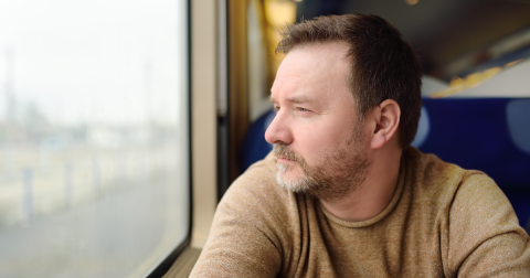 Man in beige top looks out of train window.